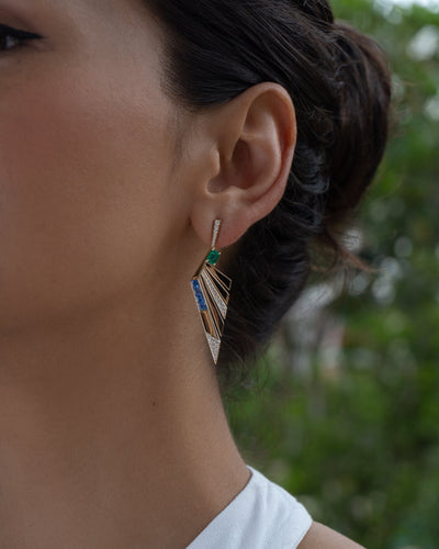 Close-up of a person wearing a silver earring with a green gemstone against a blurred natural background.